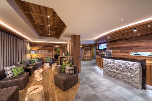 A modern interior with wooden accents, a reception desk, and a cozy seating area with sofas and a fireplace. - Hotel Sporting Ravelli (Mezzana)