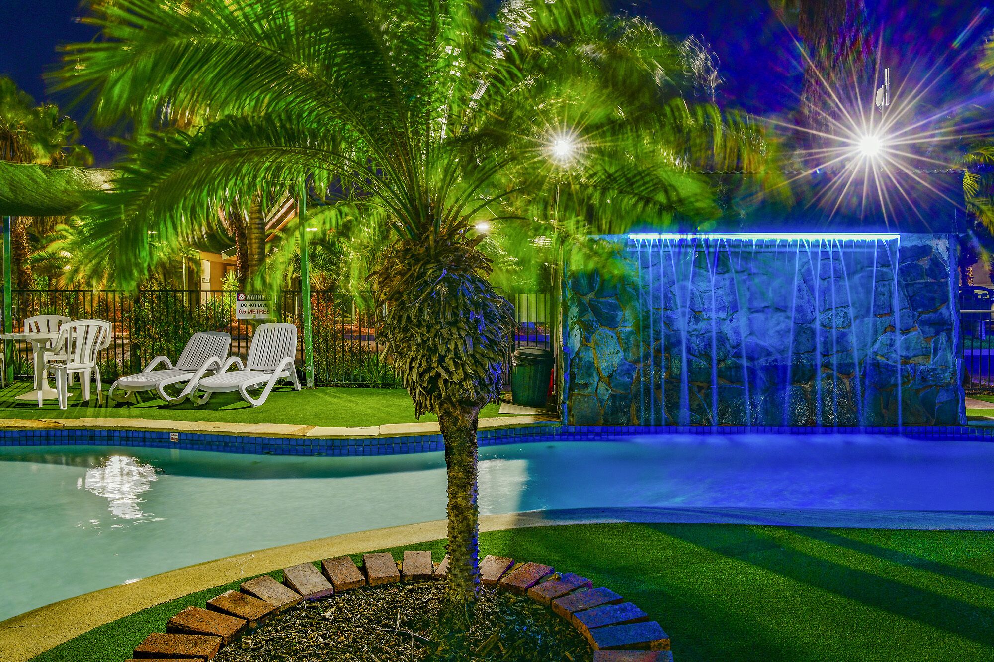 A pool area with lounge chairs, a palm tree, and a waterfall feature.