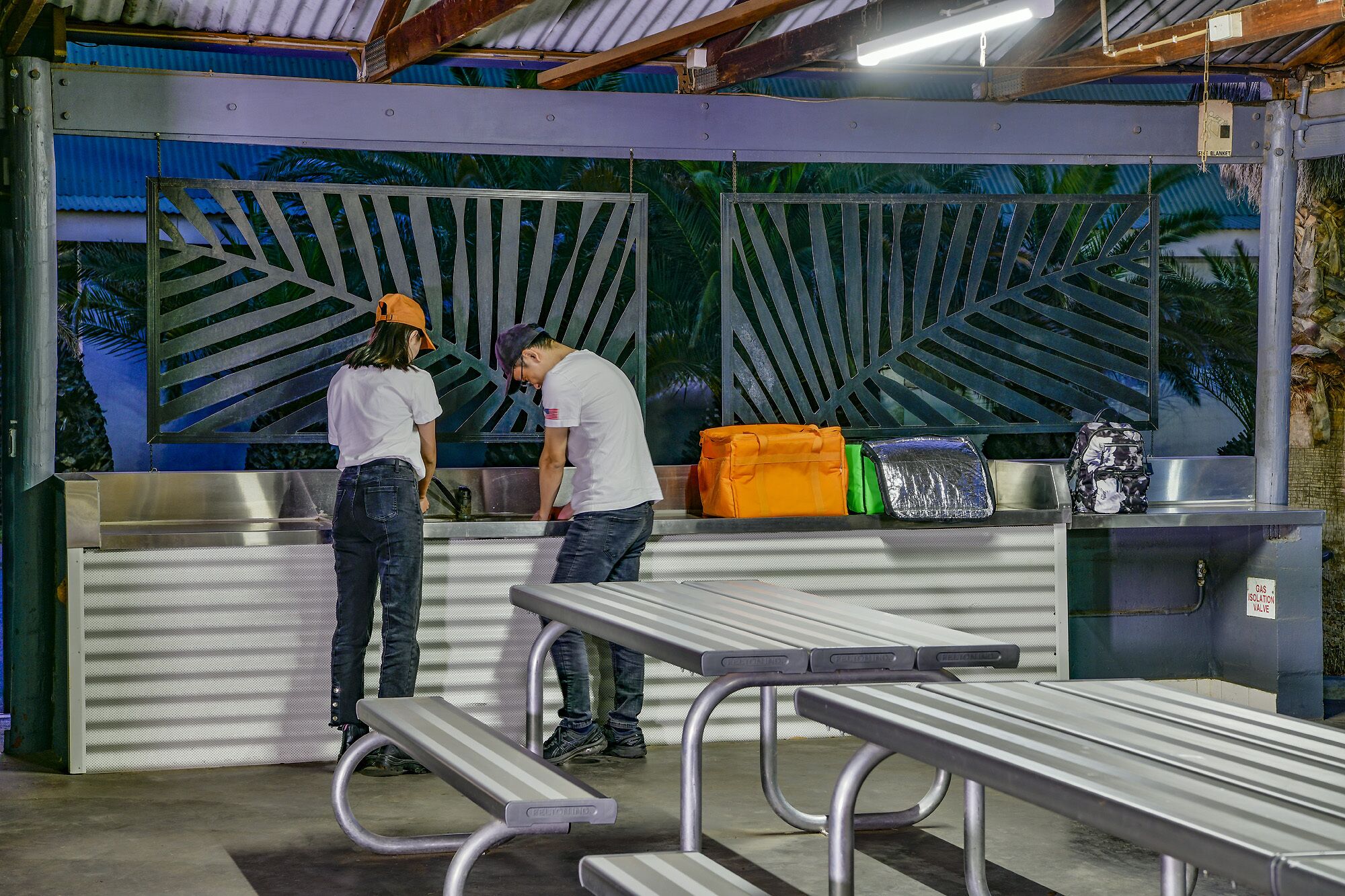 A food service area with a metal counter, benches, and a decorative metal panel with palm leaf patterns.