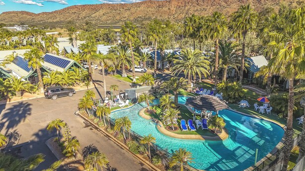 Vue aérienne d’un complexe hôtelier doté d’une piscine, de palmiers et de panneaux solaires.