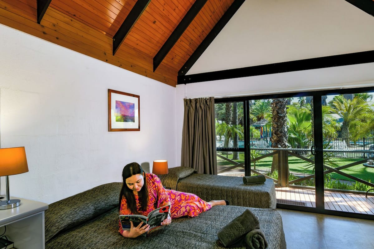 Quarto com uma janela grande, cama, área de leitura e um quadro na parede.