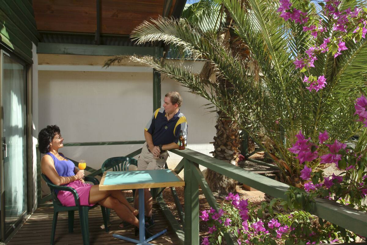 Uma área de pátio com mesa e cadeiras, cercada por plantas e uma palmeira.