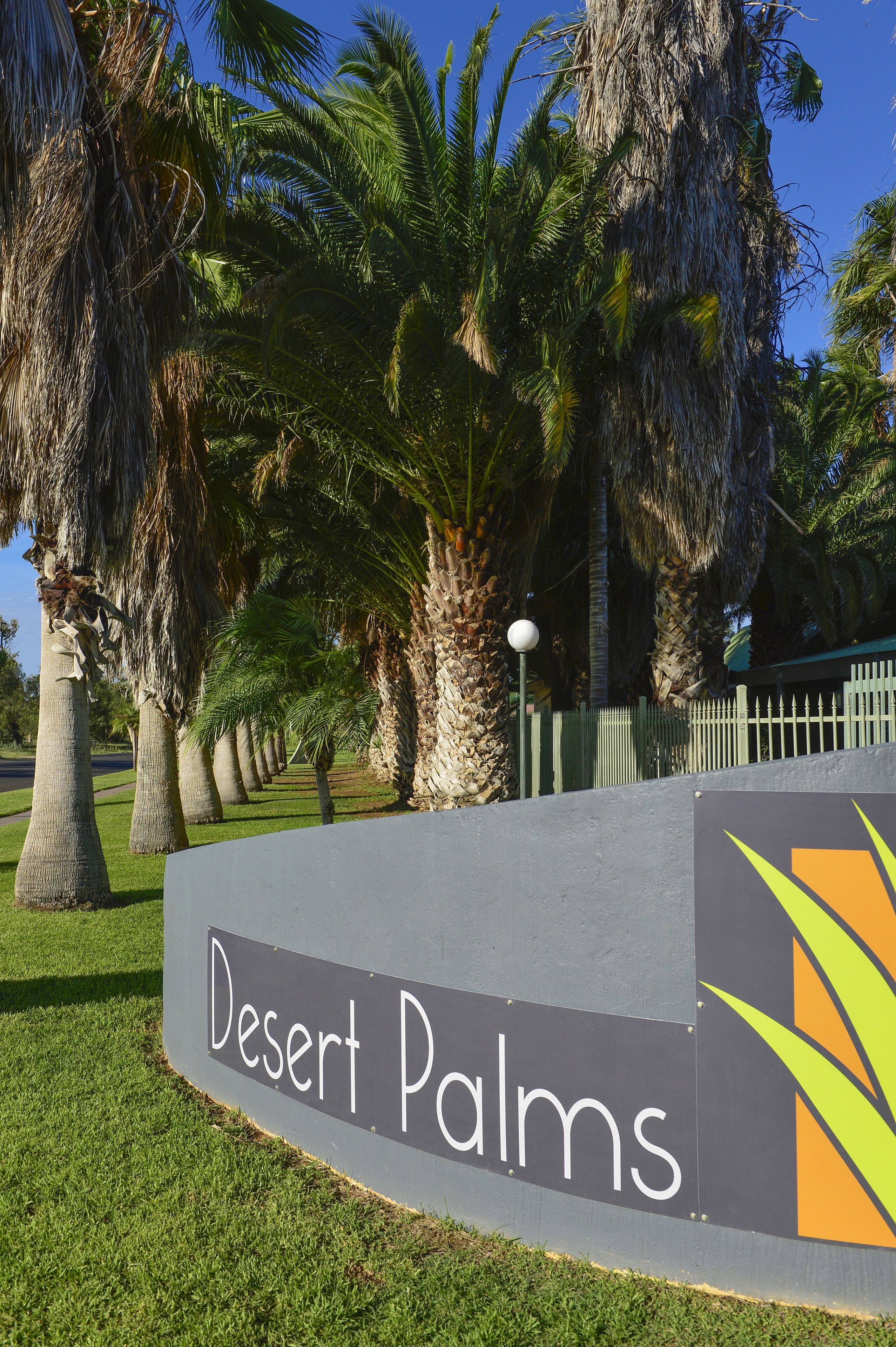 A sign for 'Desert Palms' with a clear view of palm trees and a well-maintained lawn.
