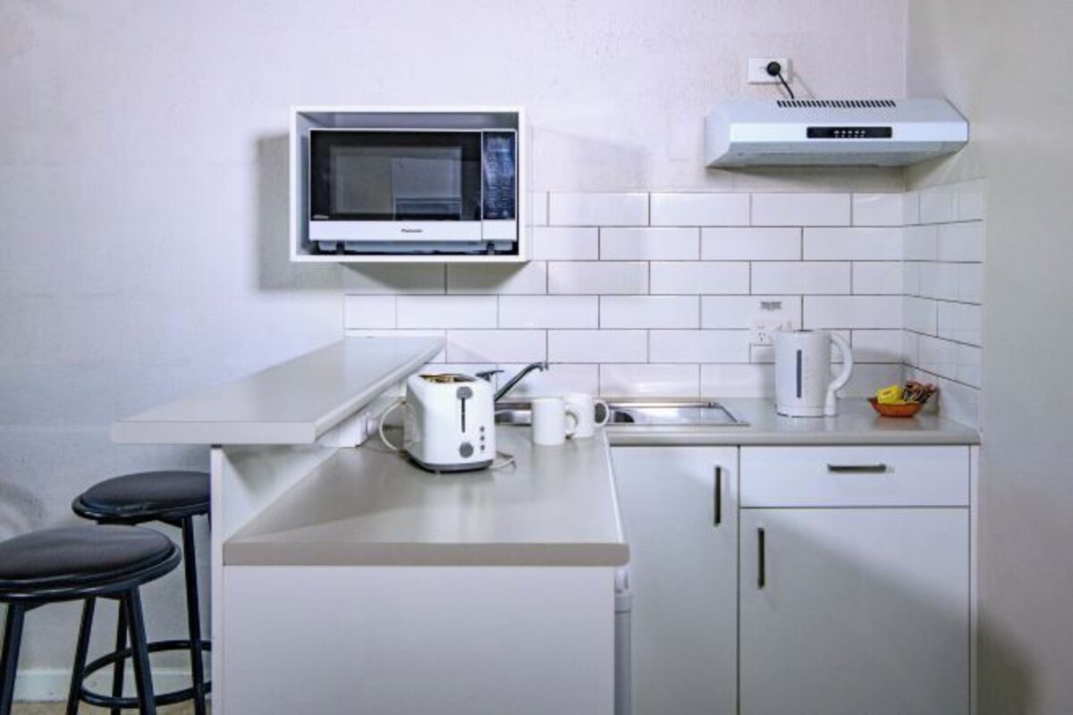 A compact kitchenette with a microwave, toaster, kettle, and a small sink.