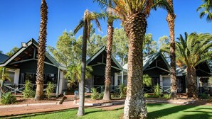 Une rangée de chalets de style bungalow, avec des palmiers devant, entourés d’une pelouse bien entretenue.