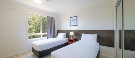 A hotel room with two beds, a window with curtains, a ceiling fan, and a framed picture on the wall.