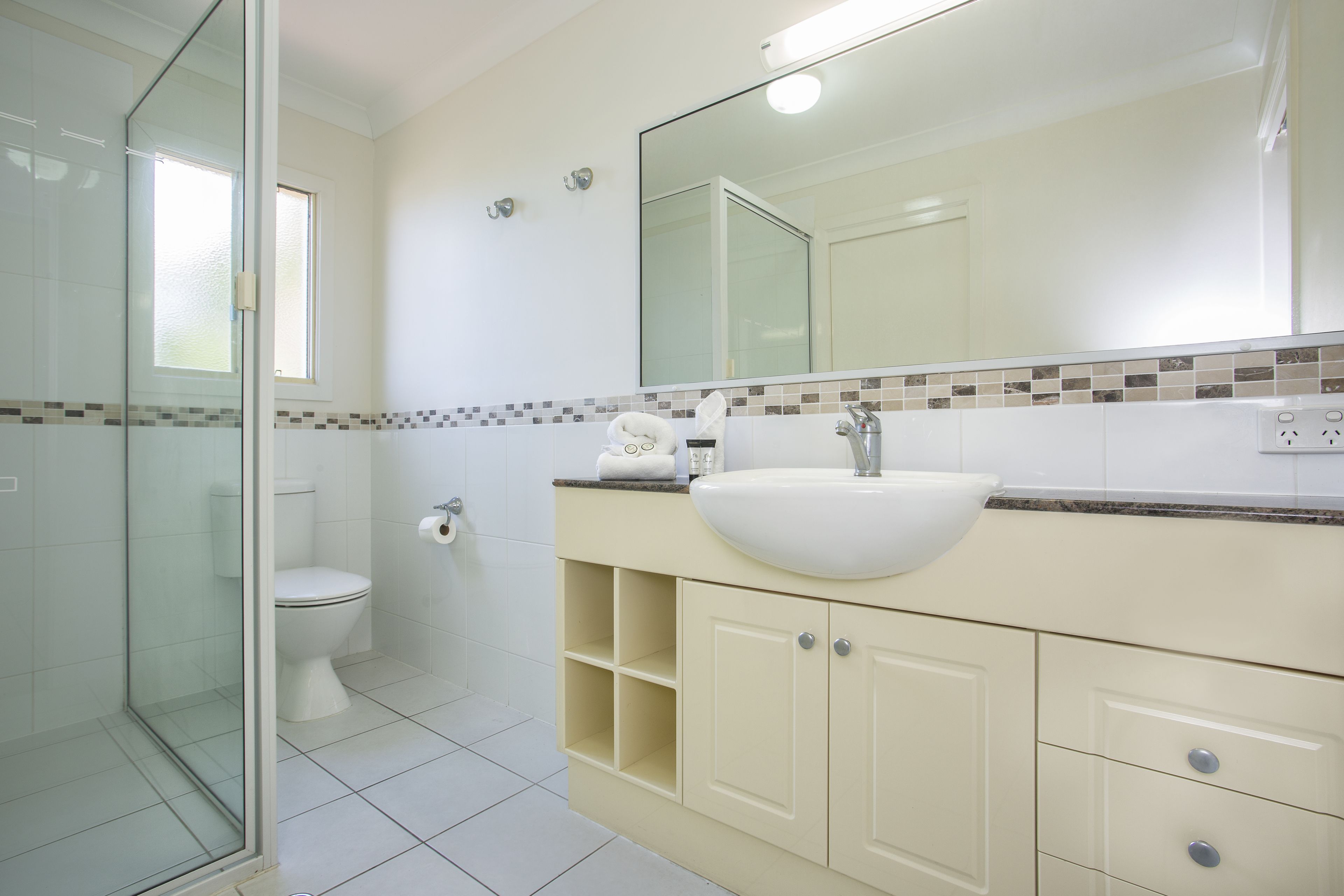 A bathroom with a glass shower enclosure, a toilet, a sink with a mirror above it, and a tiled backsplash.