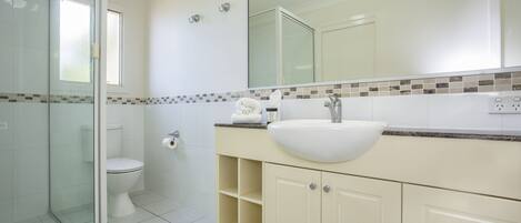 A bathroom with a glass shower enclosure, a toilet, a sink with a mirror above it, and a tiled backsplash.