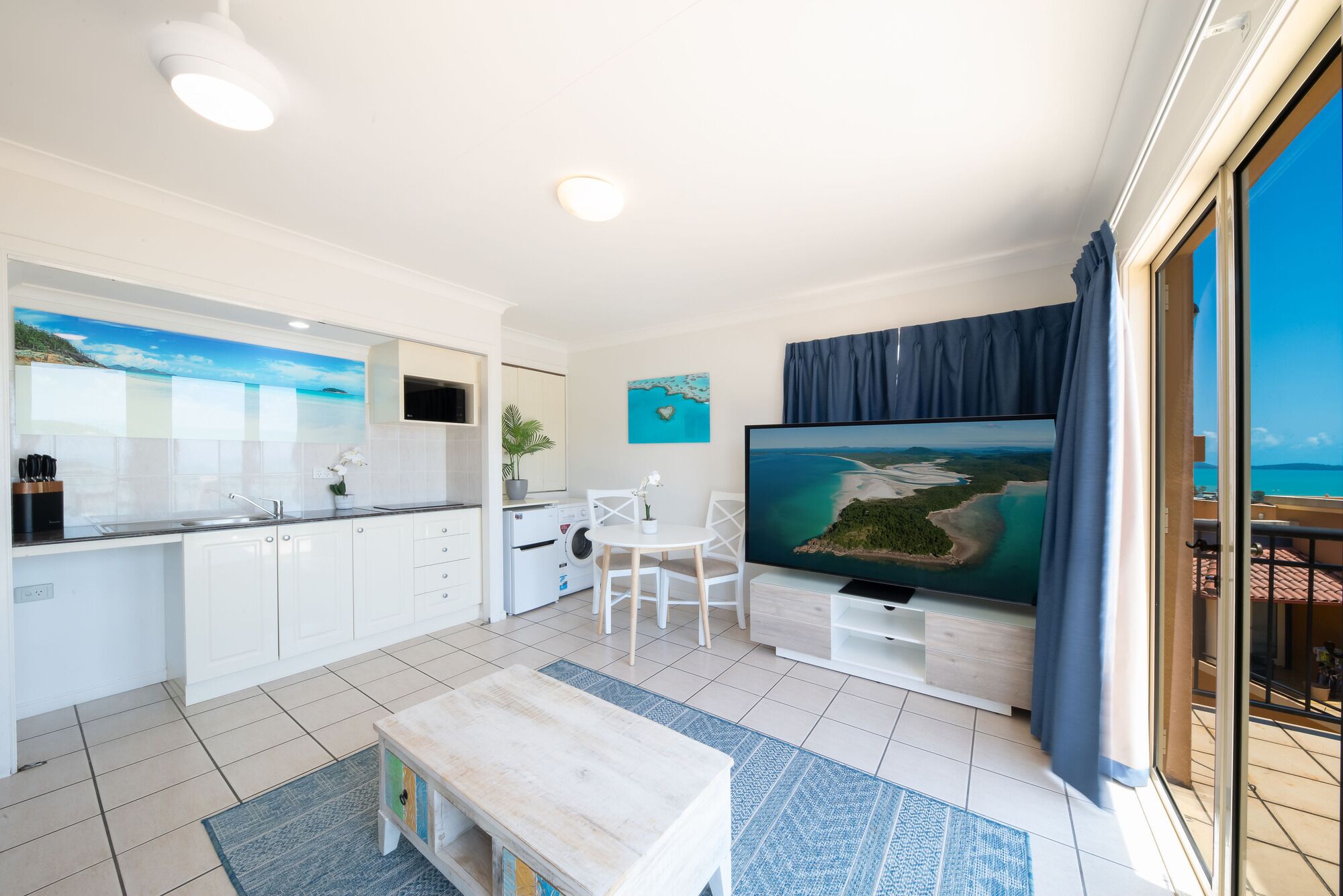 Una sala de estar moderna con cocina, televisor de pantalla plana y balcón con vista al mar.