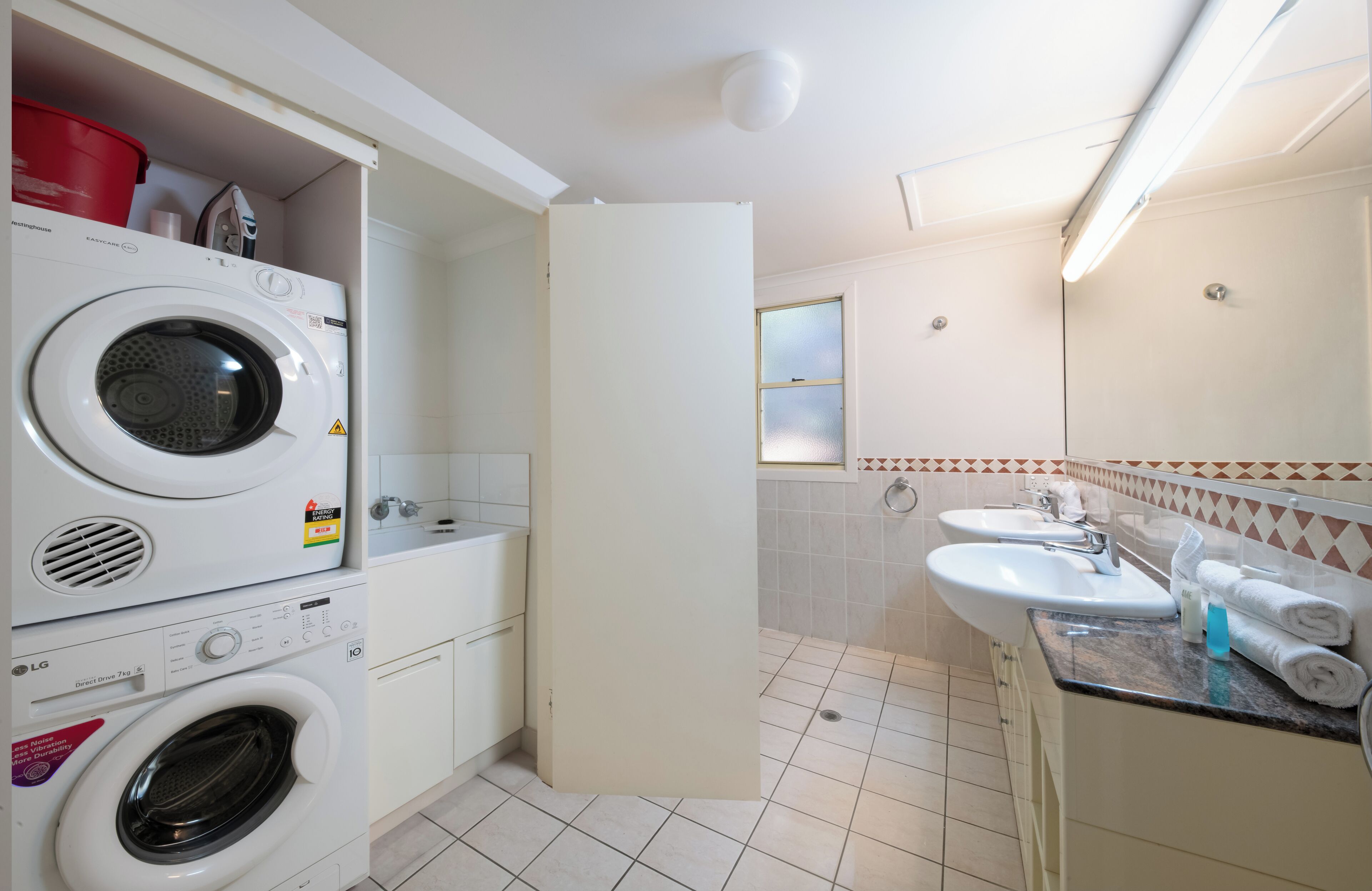 A laundry area with stacked washers and dryers, a sink with a mirror, and a tiled floor.