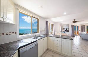 A modern kitchen with a view of the sea, white cabinetry, and a dishwasher. - Martinique Whitsunday (Airlie Beach)