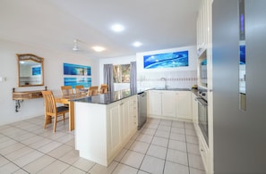 A modern kitchen with white cabinets, a central island, and a dining area with wooden chairs. - Martinique Whitsunday (Airlie Beach)