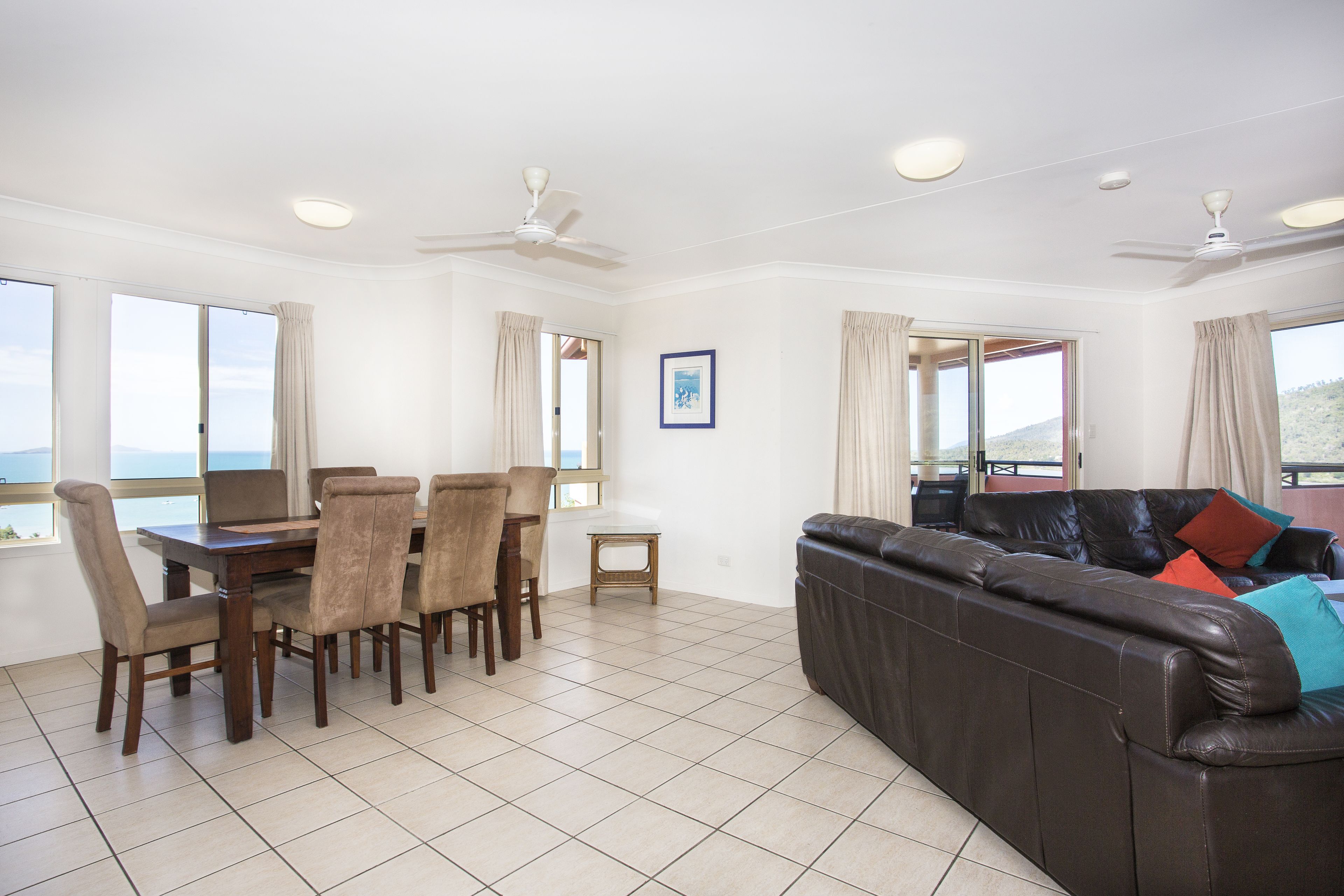 A spacious living area with a dining table and chairs, a leather sofa, and large windows offering a view.