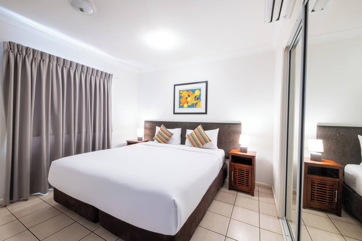 Une chambre d’hôtel avec un grand lit, une tête de lit agrémentée de deux oreillers, une table de chevet avec une lampe, un tableau encadré au mur et une porte coulissante.