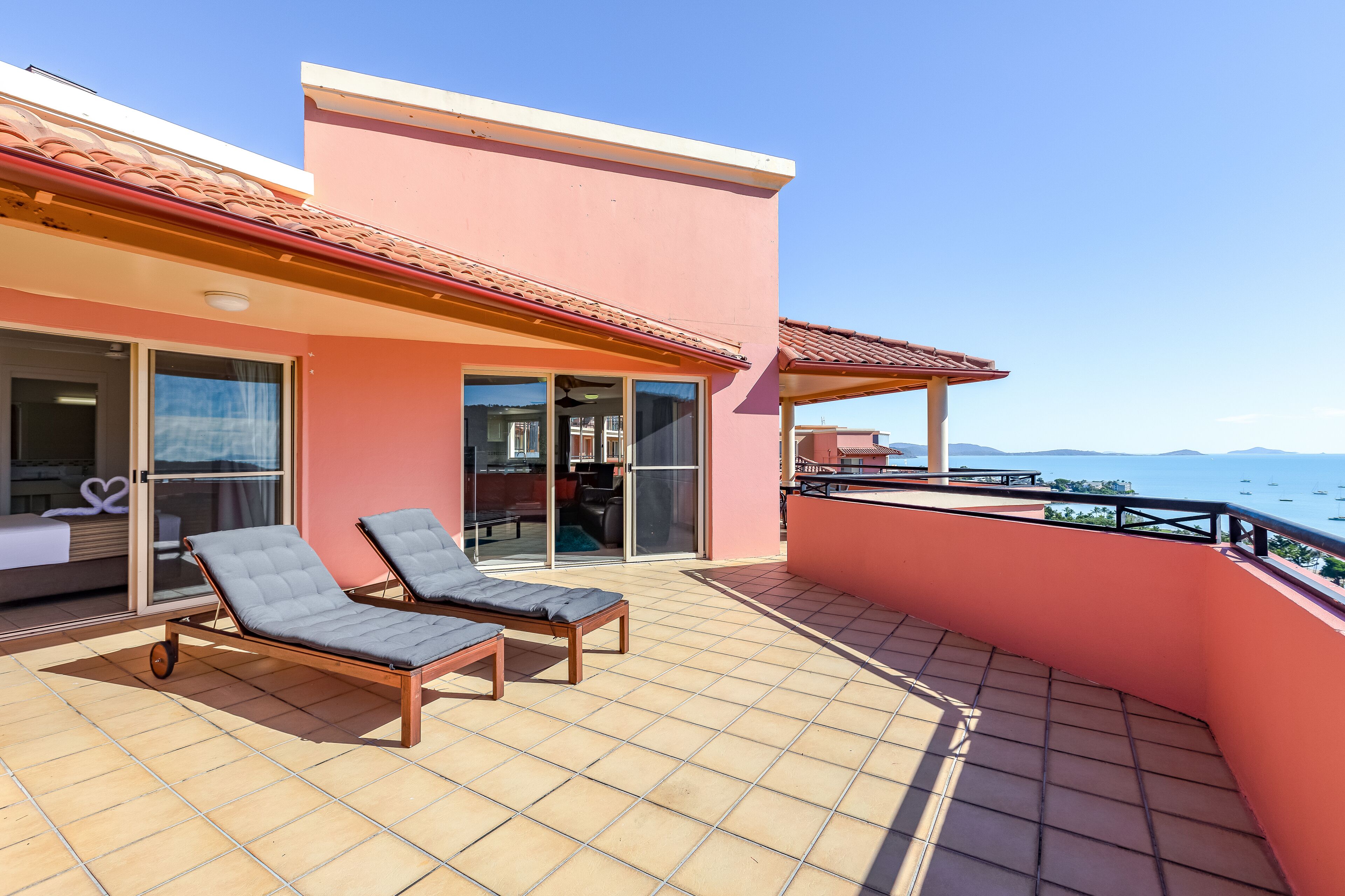 Ein Balkon mit zwei Lounge-Sesseln, einer Glastür zu einem Innenraum und Blick aufs Meer.