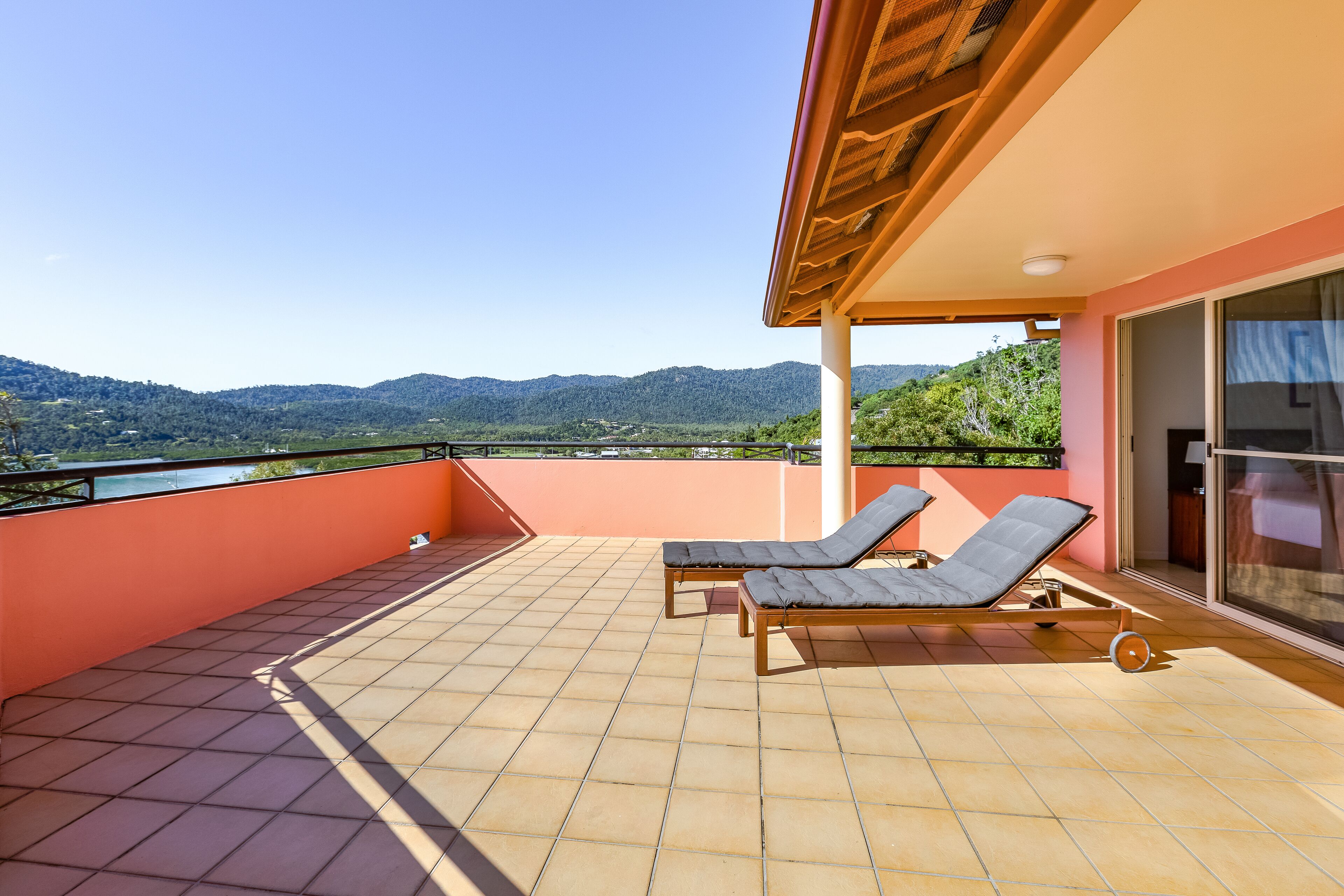 A balcony with two sun loungers, a tiled floor, and a view of green hills.