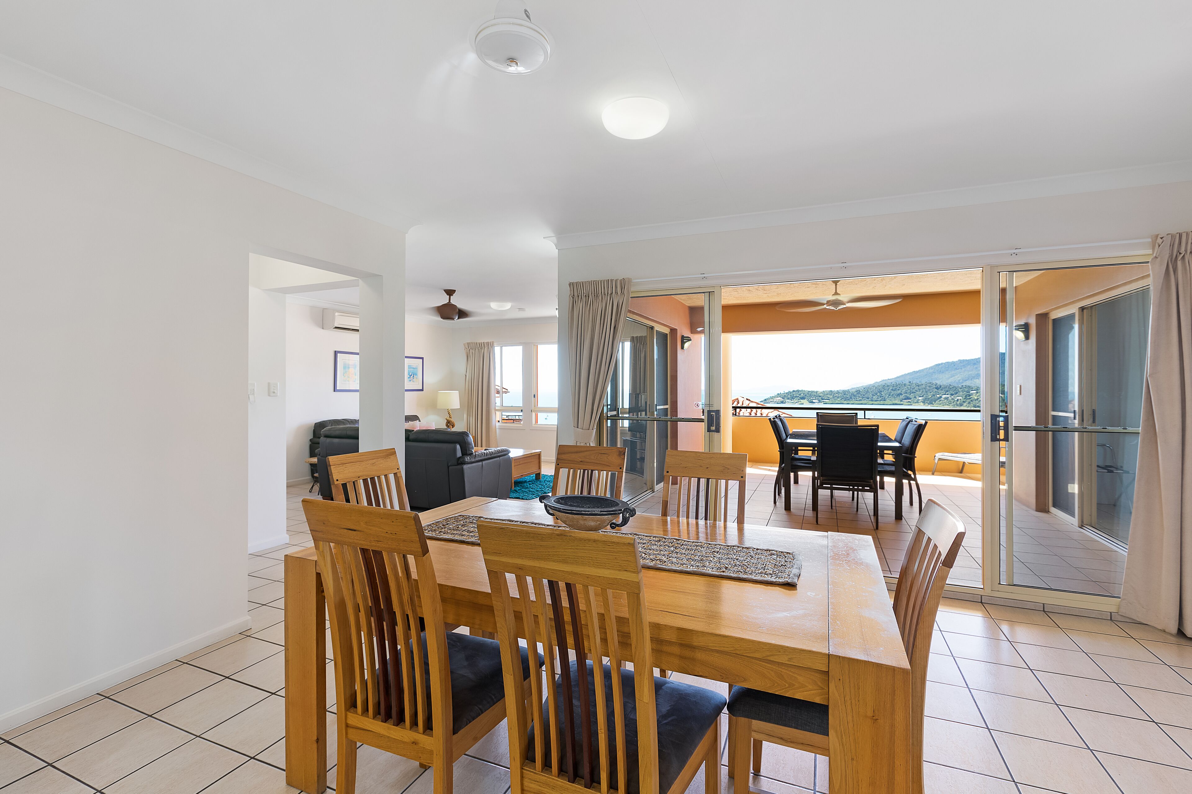 A dining area with a wooden table and chairs, a ceiling fan, and a view of the outdoors.