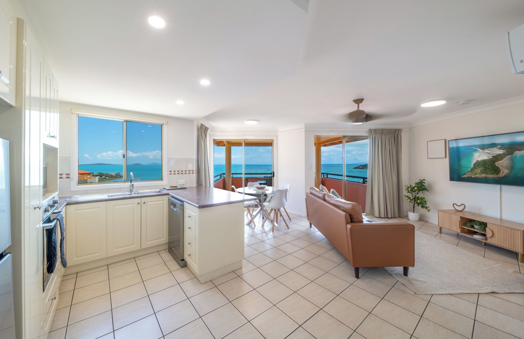 A modern living space with a kitchen, dining area, and a balcony with a view of the sea.