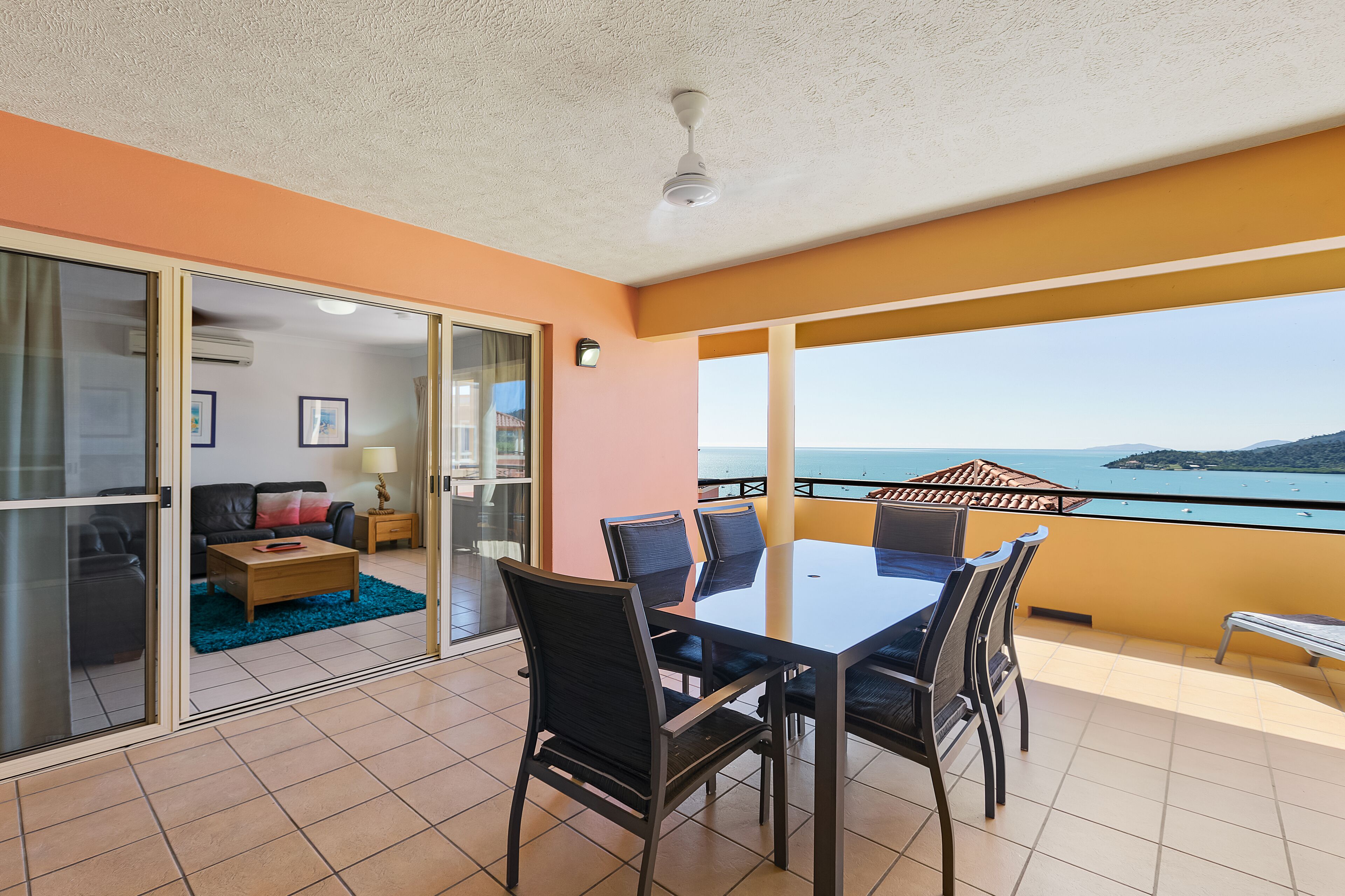 A balcony with a table and chairs, a sofa, and a view of the sea.
