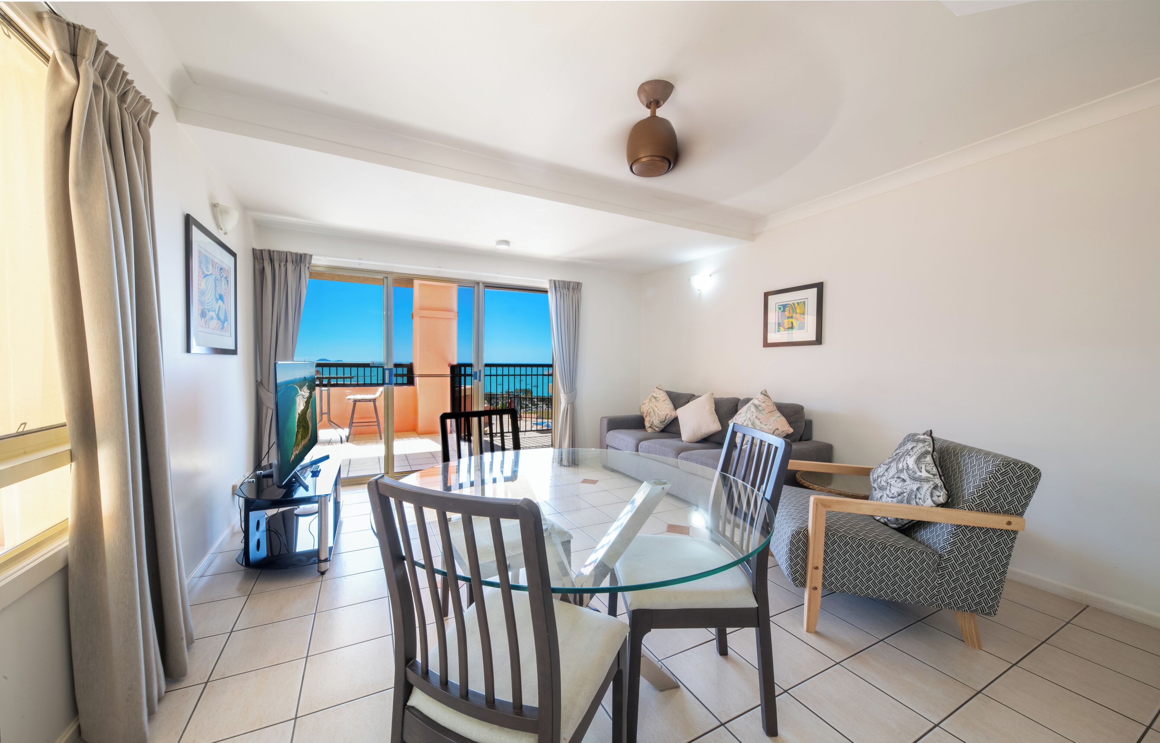 Una sala de estar moderna con una mesa de comedor de cristal, dos sofás y un balcón con vistas.