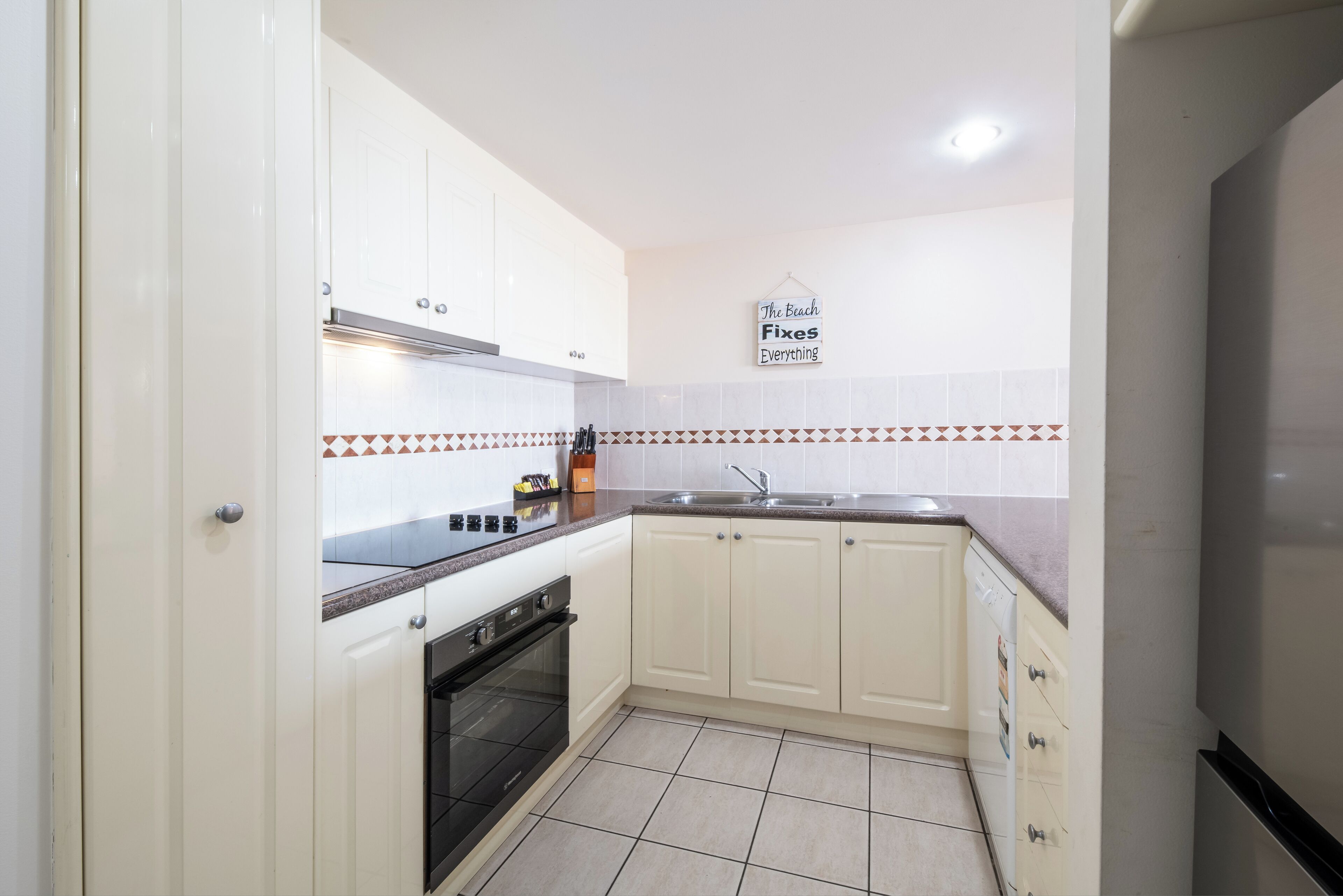 A kitchen with white cabinets, a black stove, a sink, and a tiled backsplash.