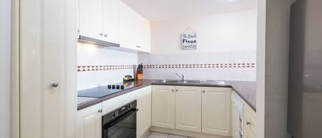 A kitchen with white cabinets, a black stove, a sink, and a tiled backsplash.