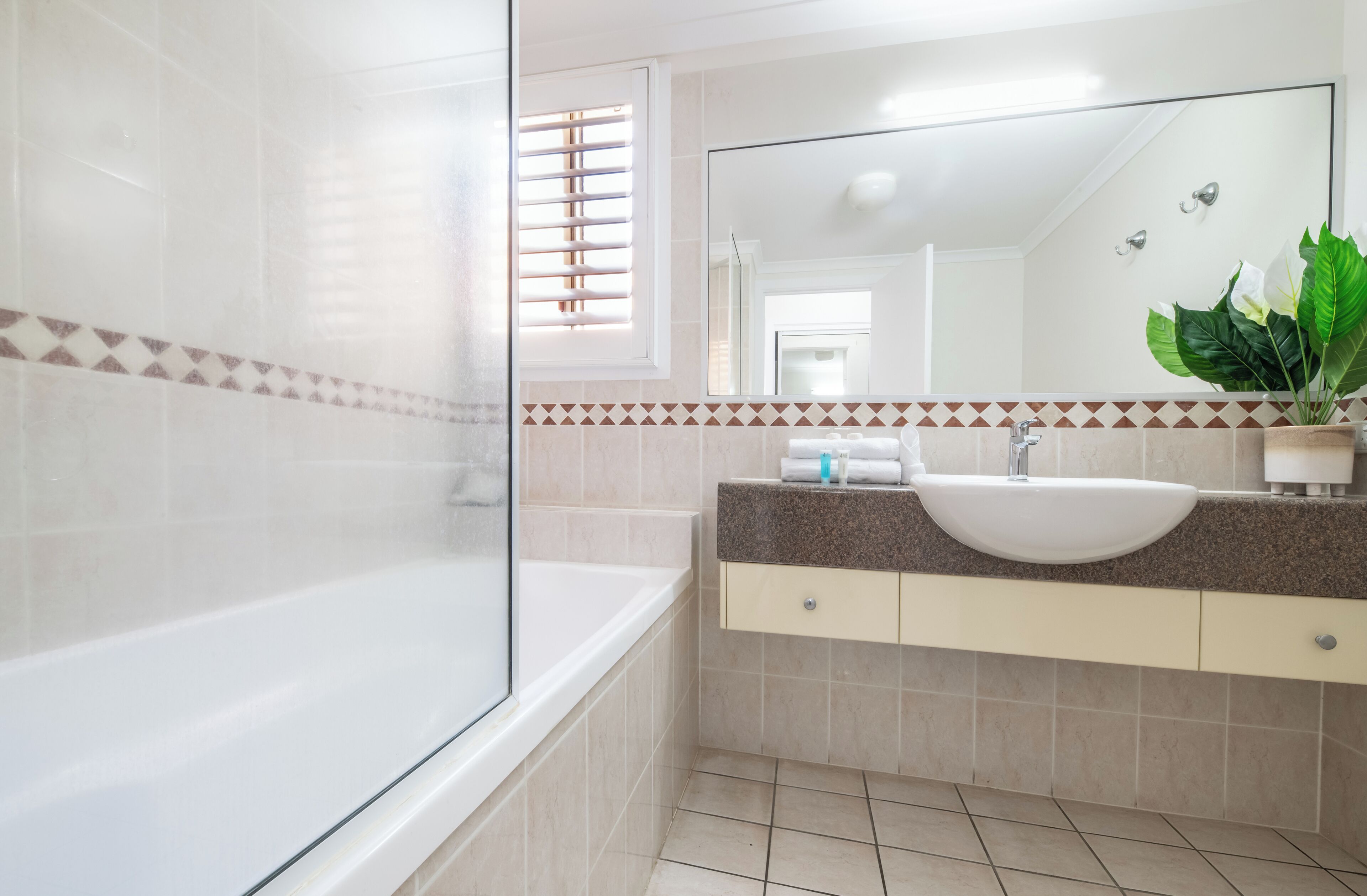 A modern bathroom with a bathtub, a sink with a large mirror, and a potted plant.