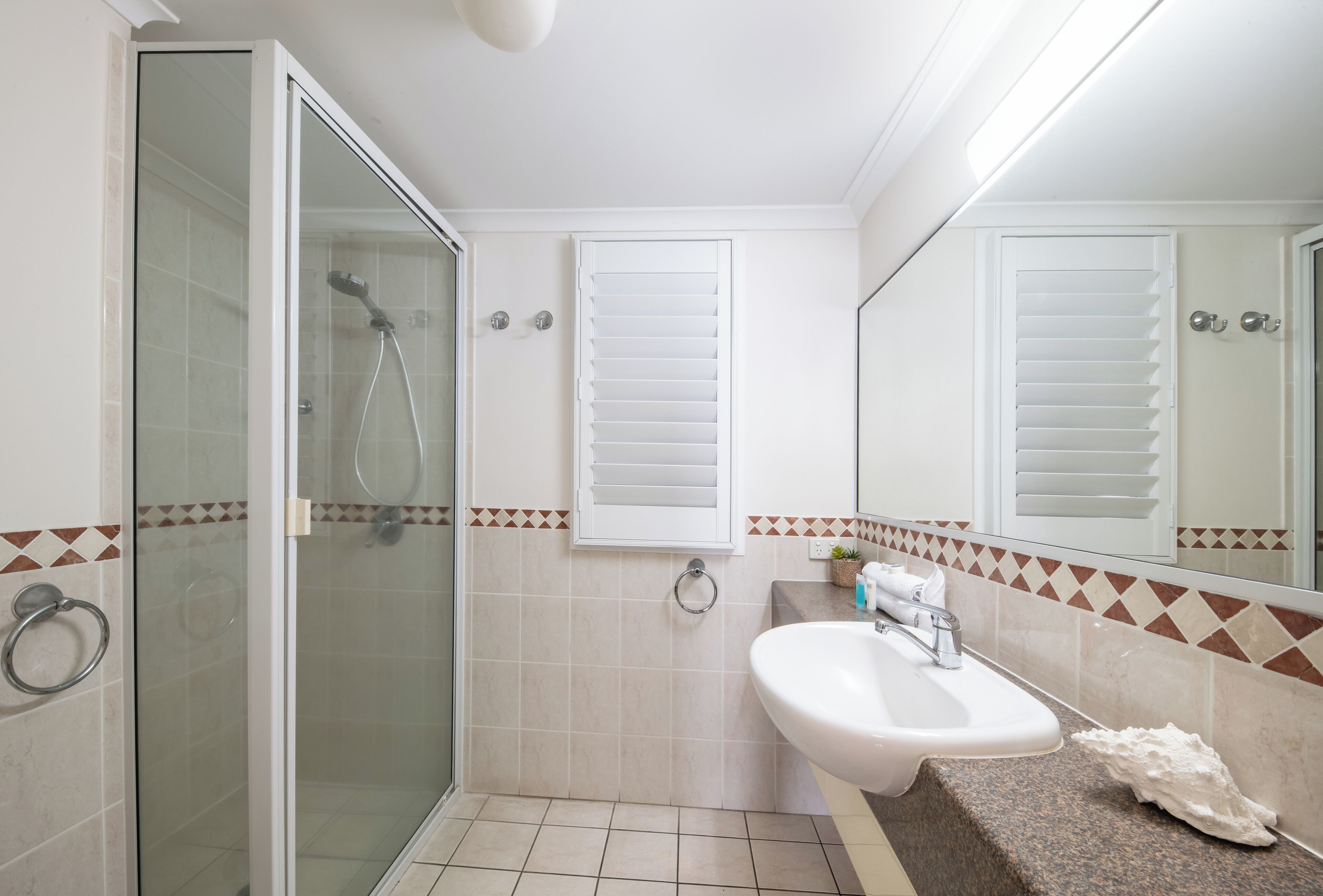 A bathroom with a glass-enclosed shower, a sink with a countertop, and a mirror above the sink.