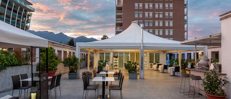 An outdoor patio area with tables and chairs, a white tent, and a view of a mountain range.