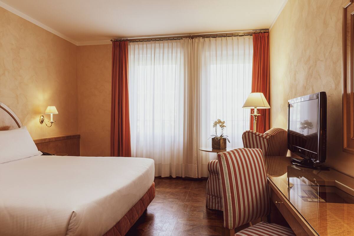 Een hotelkamer met een groot bed, een televisie, een bureau met lamp en een stoel.