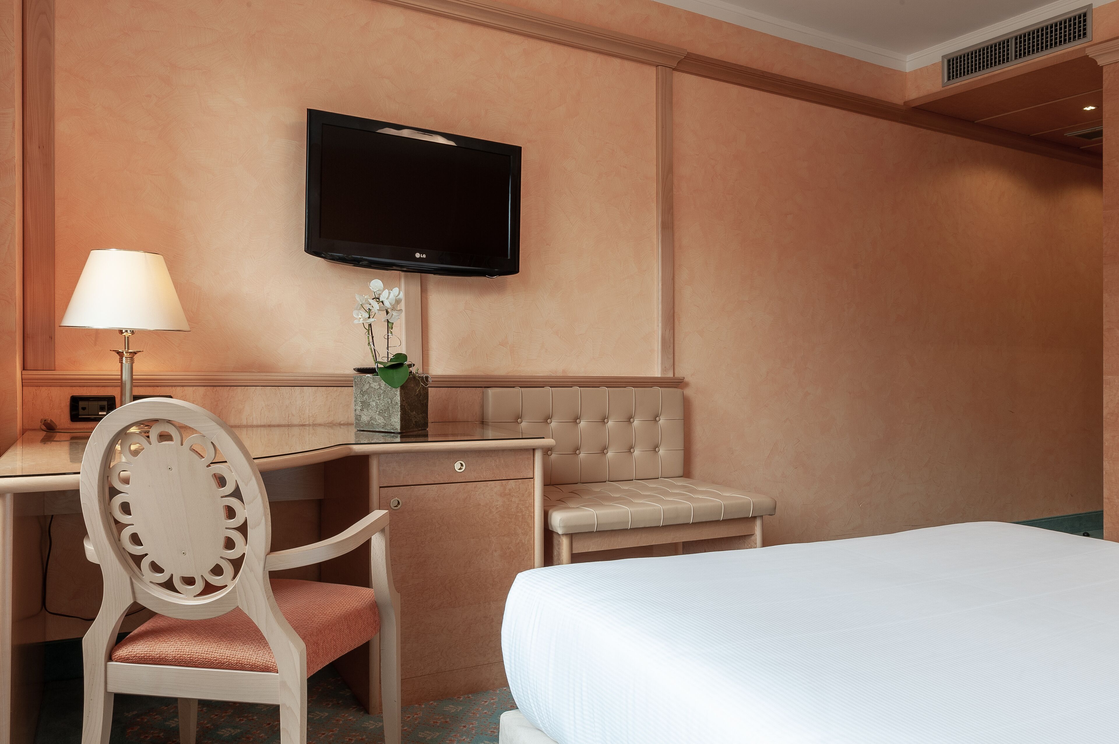 Een hotelkamer met een bed, een bureau met lamp, een stoel, een televisie en een klein bankje.