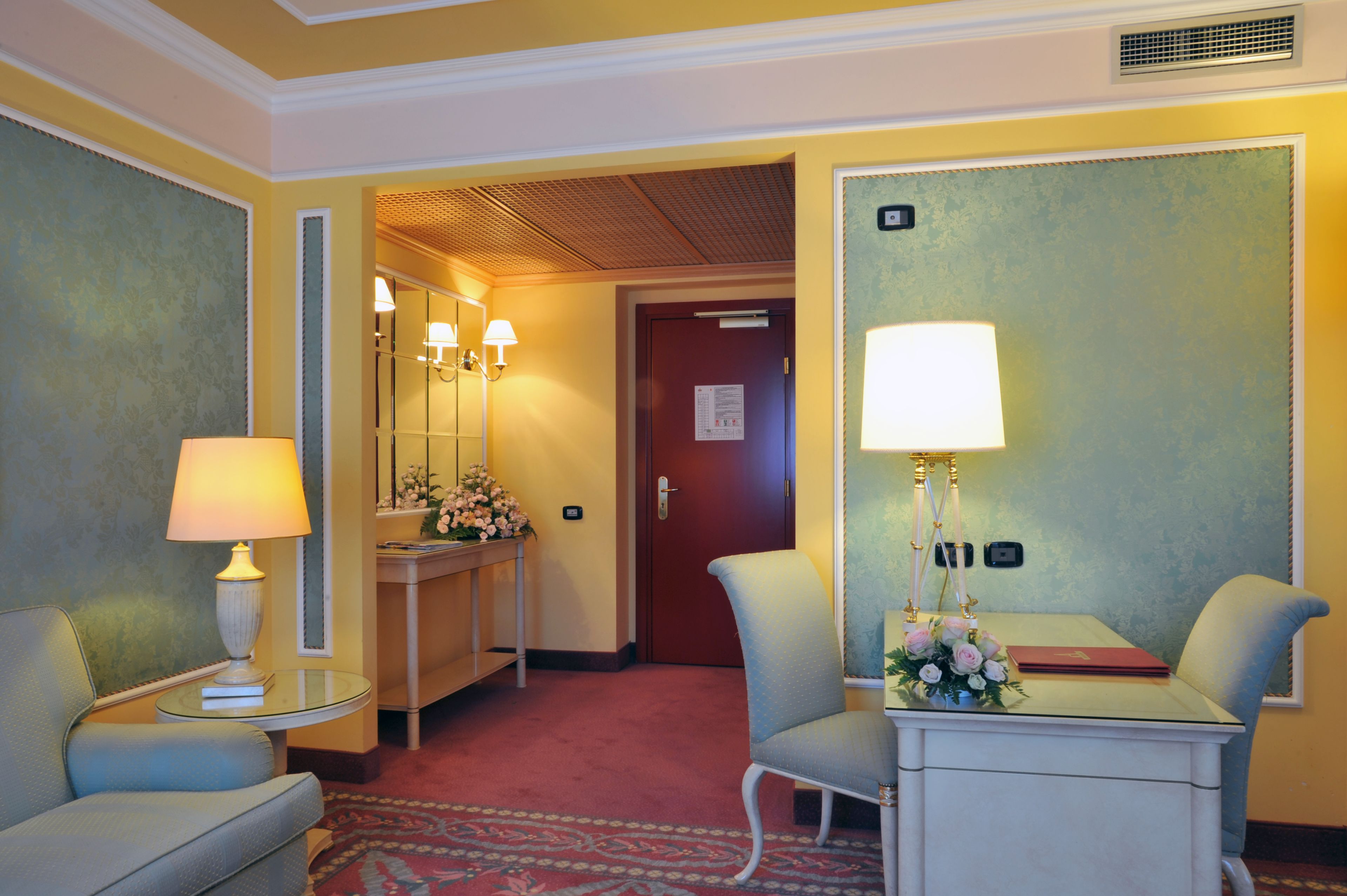 A hotel room with a bed, a desk, a chair, a lamp, a mirror, and a door.