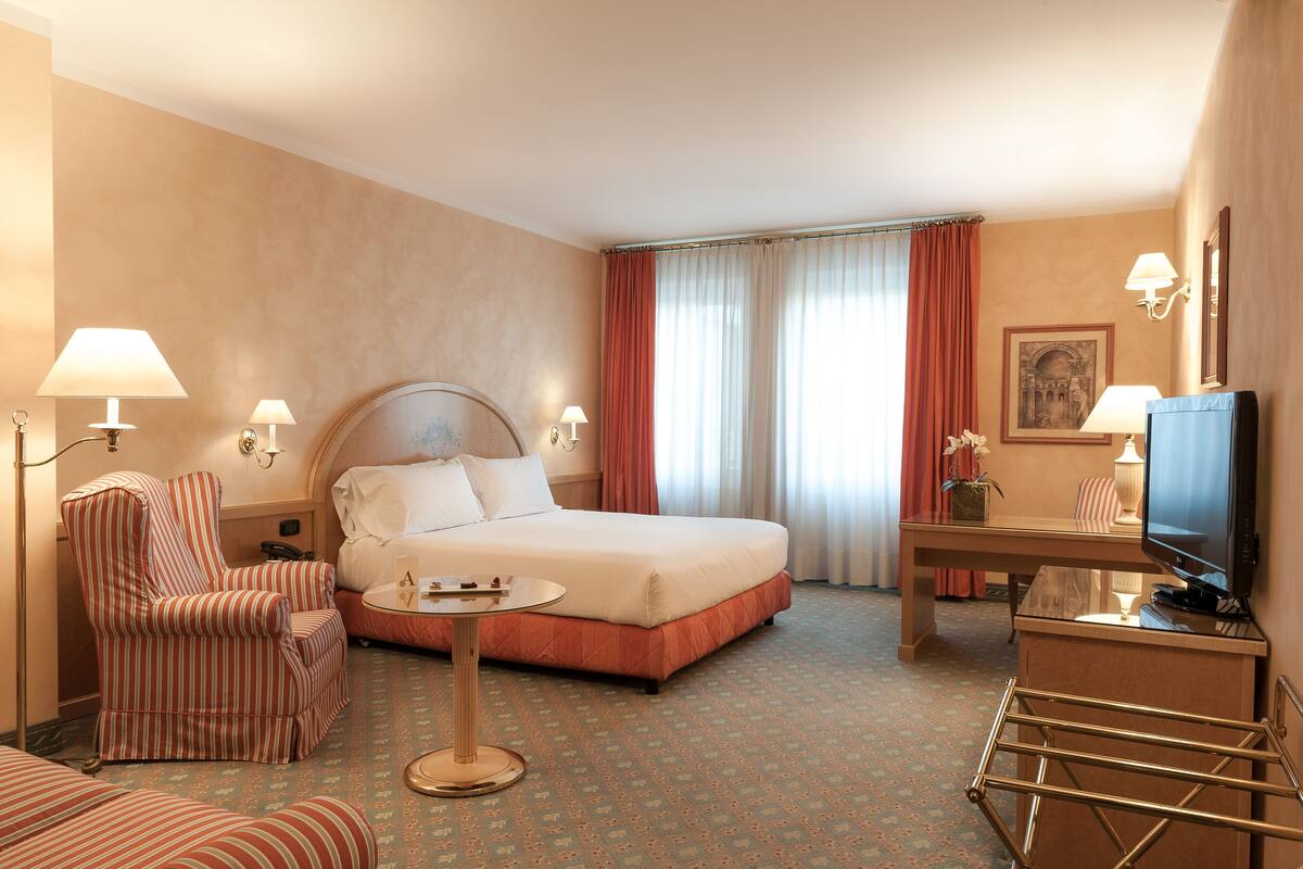 Een hotelkamer met een bed, een stoel, een bureau, een televisie en een lamp.