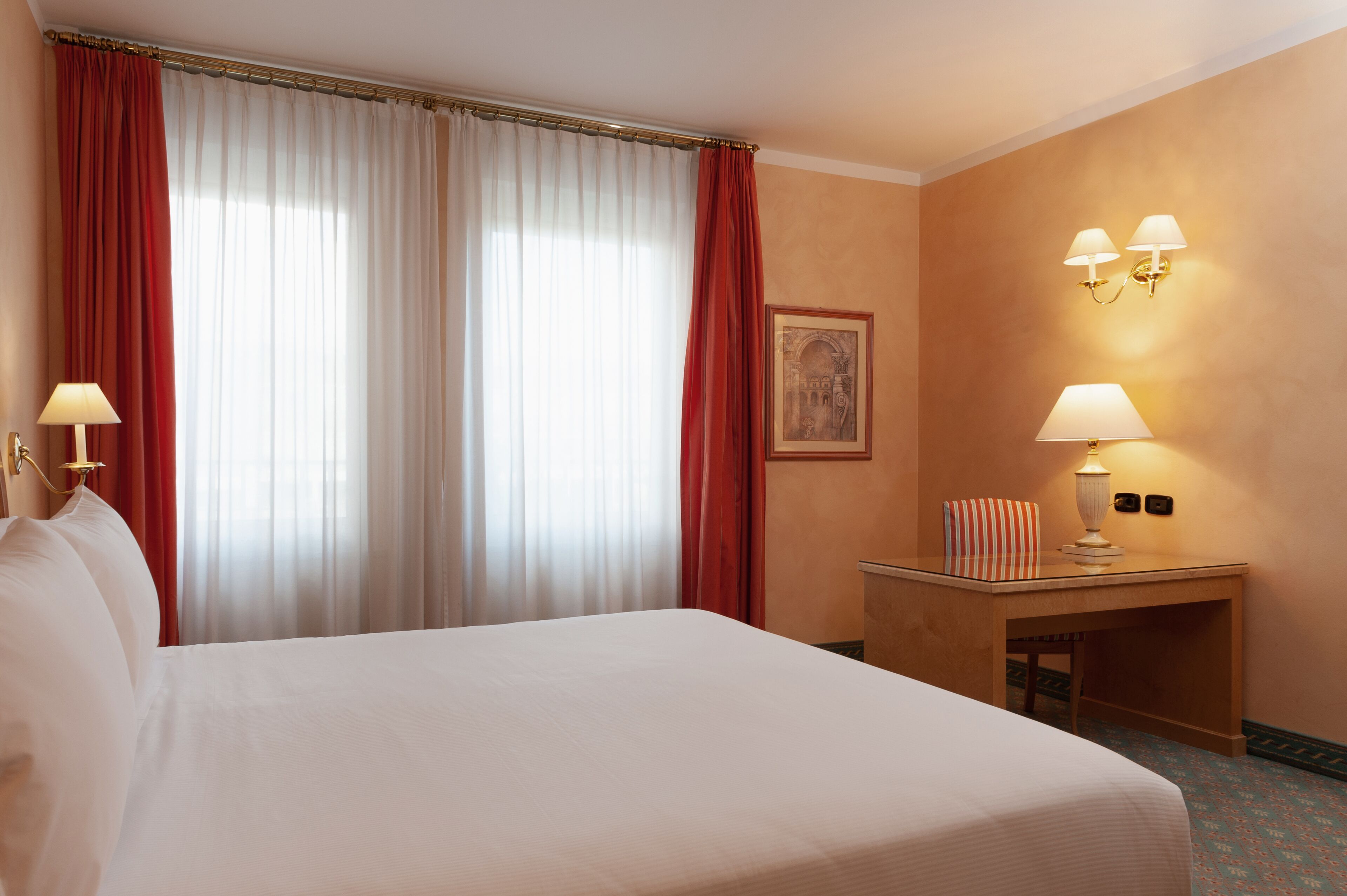 Una habitación de hotel con una cama grande, un escritorio con lámpara y un cuadro en la pared.