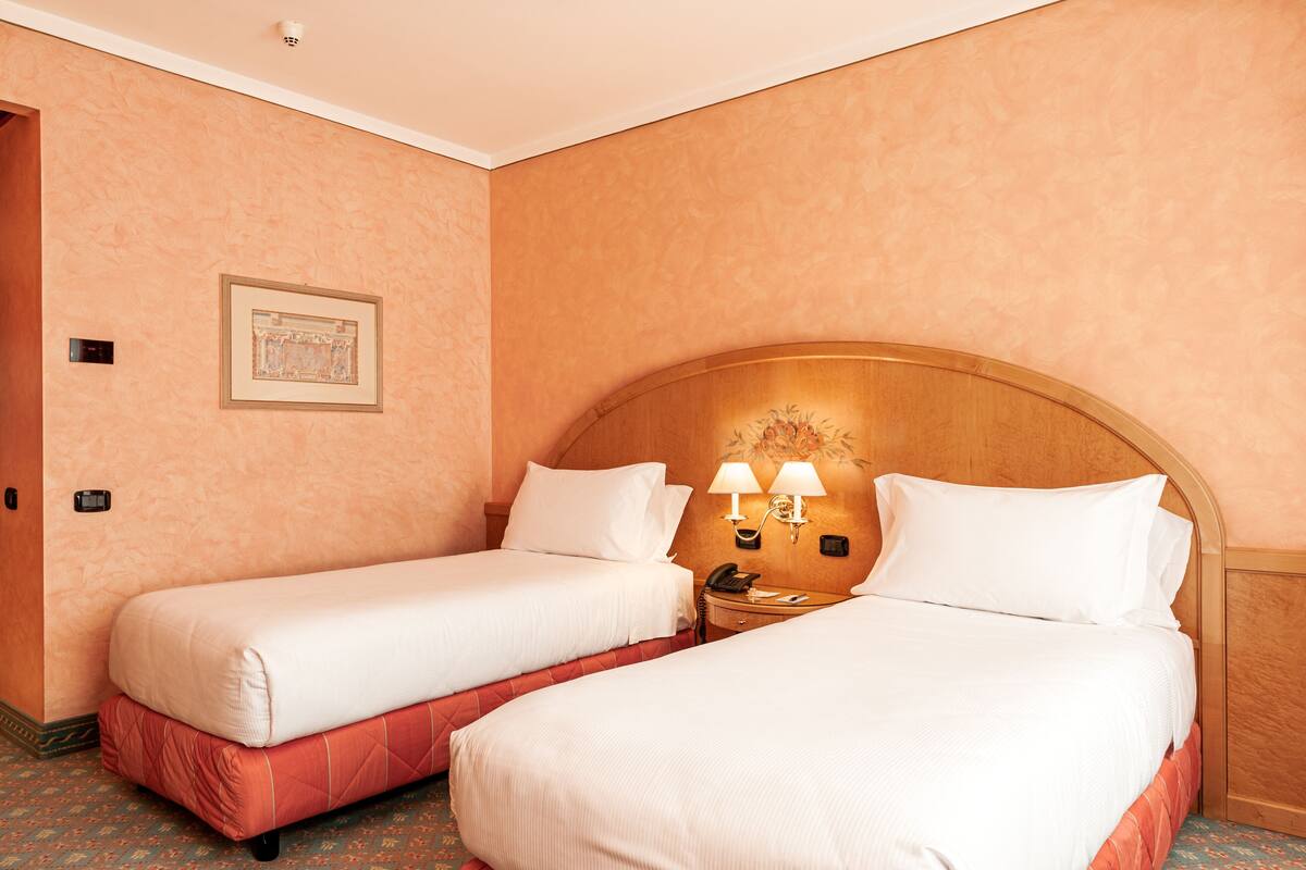 Een hotelkamer met twee bedden, een houten hoofdbord, een nachtkastje met lampen en een ingelijst schilderij aan de muur.