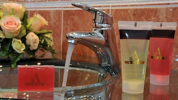 A bathroom with a chrome faucet, a vase of roses, and two cosmetic containers.