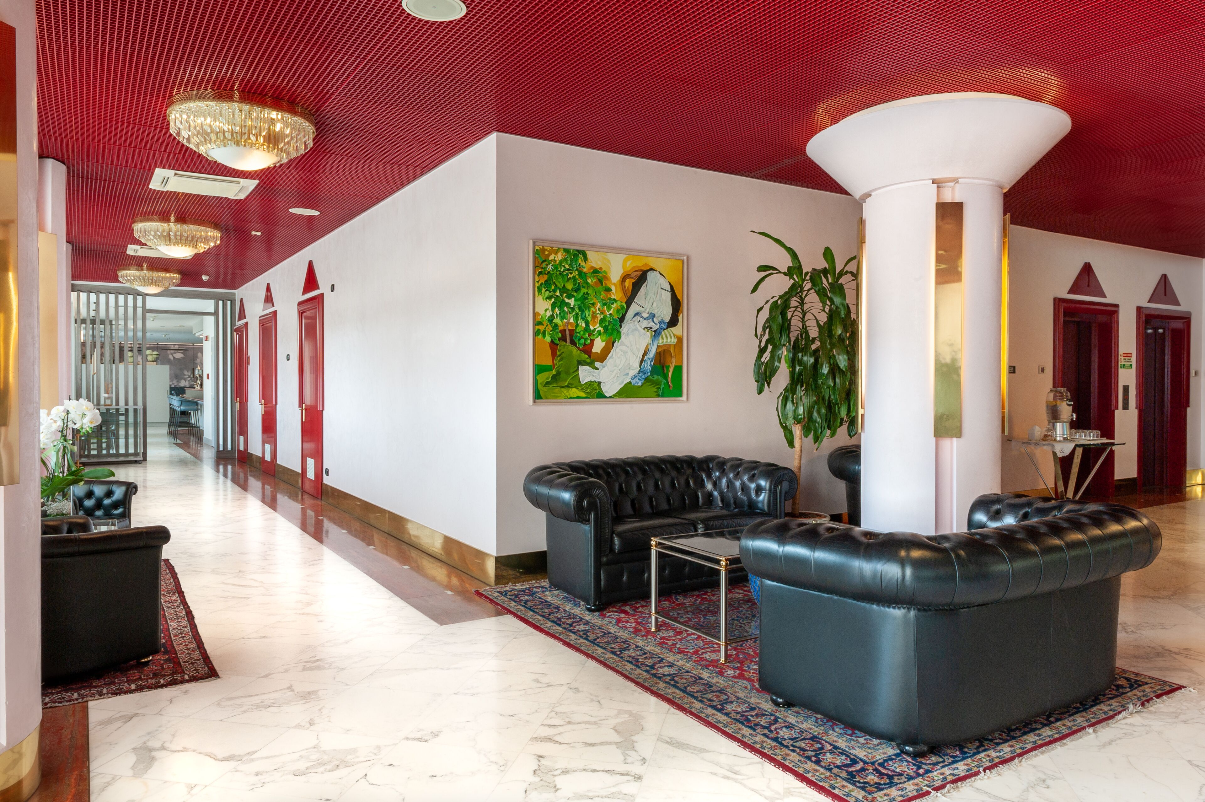 En rummelig lobby med rødt loft, en sort lædersofa, et stort maleri og en potteplante.