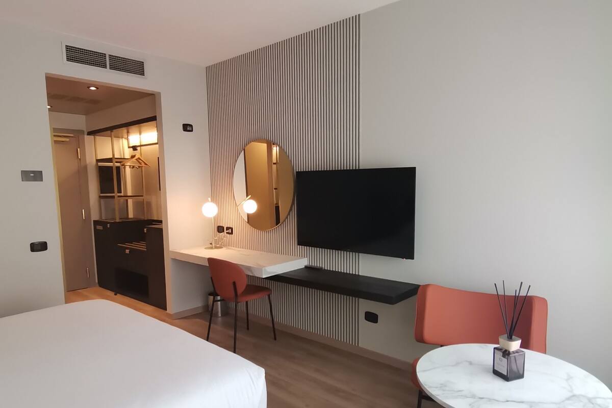 Een hotelkamer met een bed, een bureau met stoel, een televisie en een klein tafeltje met een kaars.