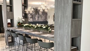 Un comedor moderno con una mesa larga, múltiples sillas, lámparas colgantes y un fondo con diseño floral.