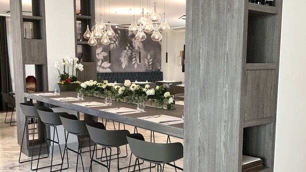 Un comedor moderno con una mesa larga, múltiples sillas, lámparas colgantes y un fondo con diseño floral.