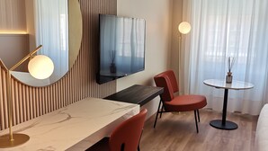 Una habitación de hotel moderna con una pared de listones de madera, un televisor de pantalla plana, una encimera de mármol, sillas rojas y una mesa redonda con un jarrón.