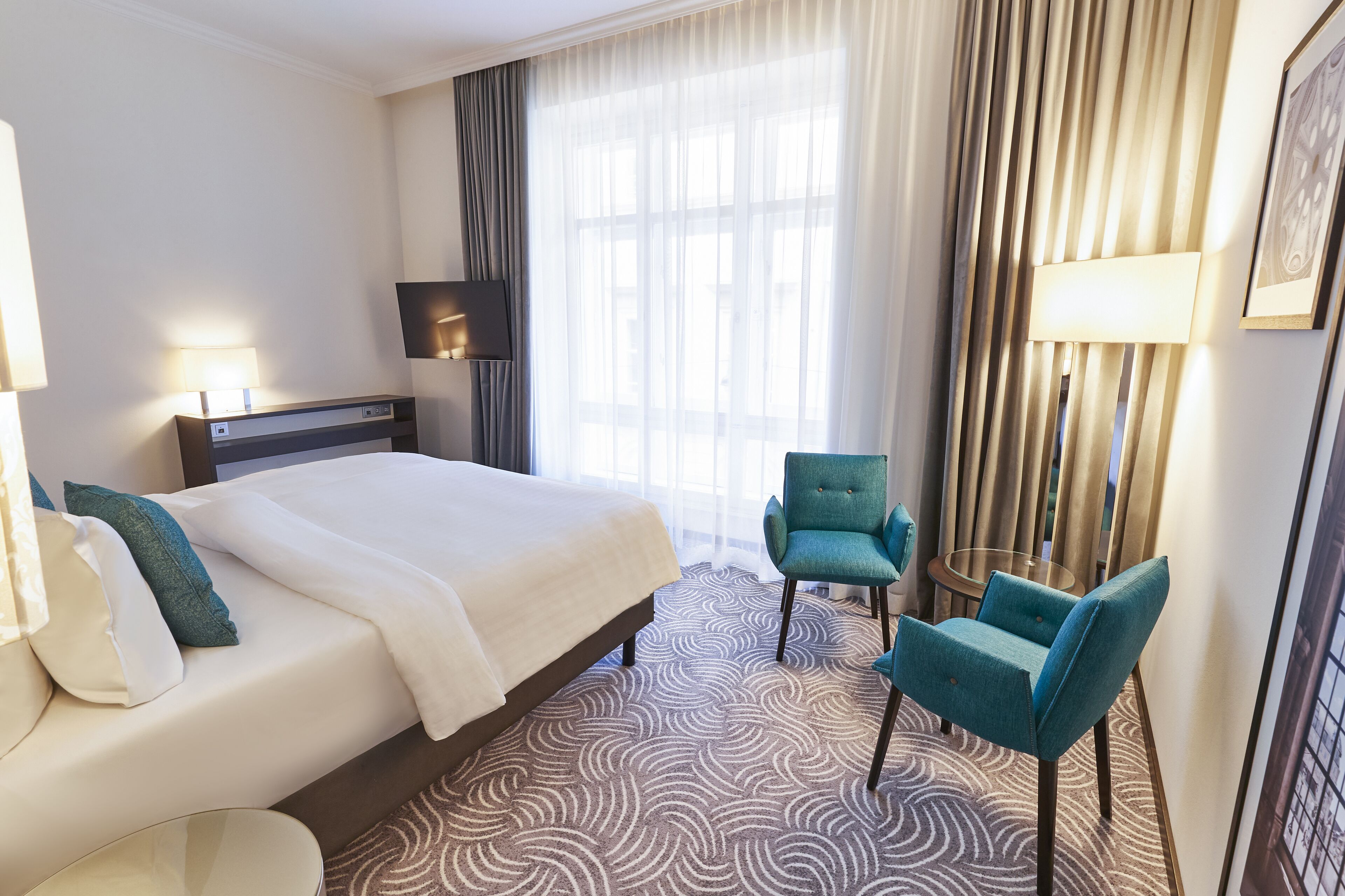 Habitación de hotel con una cama grande, dos sillas, un televisor y una ventana con cortinas.