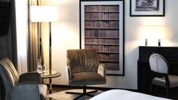 Una habitación de hotel con una cama, dos sillones, un escritorio, una estantería y dos lámparas.