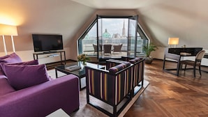 Una sala de estar moderna con sofá, televisor, zona de comedor y vistas a un paisaje urbano.