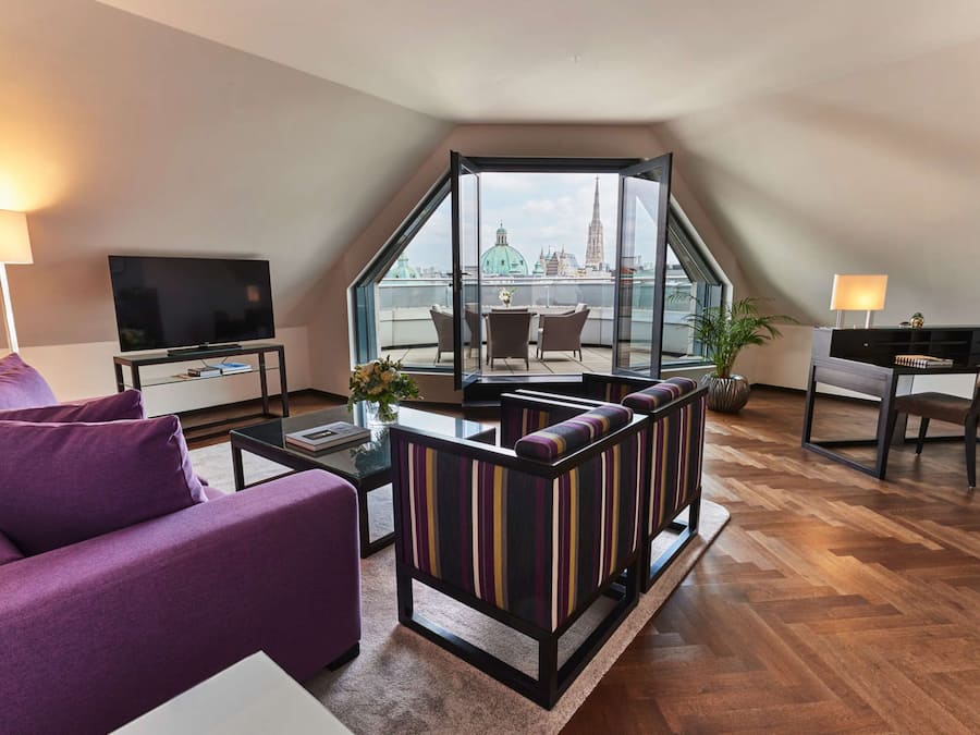 A modern living room with a sofa, a TV, a dining area, and a view of a cityscape.