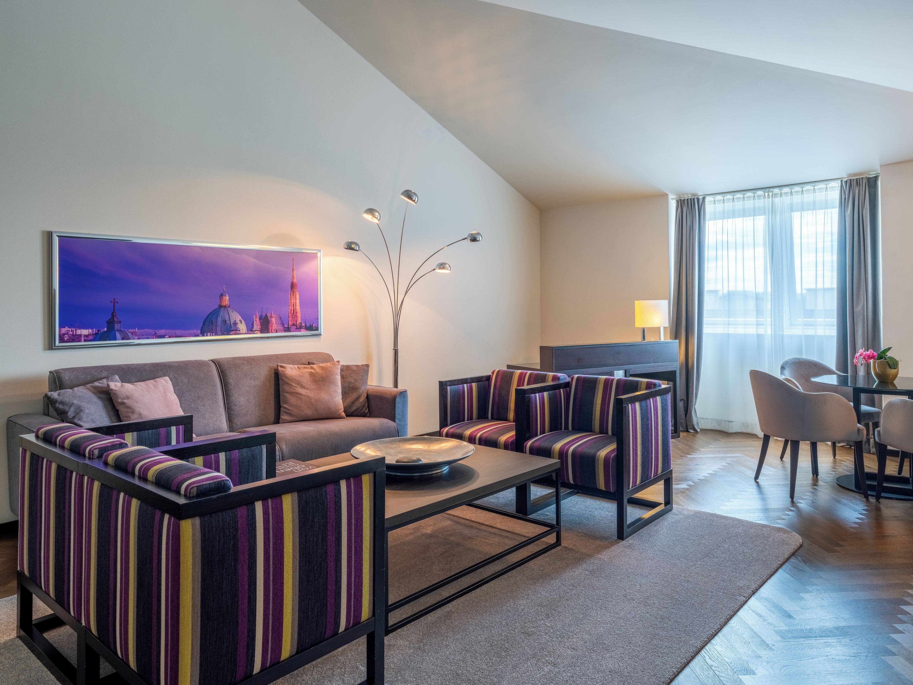 Una sala de estar moderna con sofá, sillones, una mesa de centro y televisor. Hay un cuadro en la pared y una lámpara.