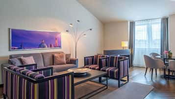 A modern living room with a sofa, armchairs, a coffee table, and a TV. There is a painting on the wall and a lamp.