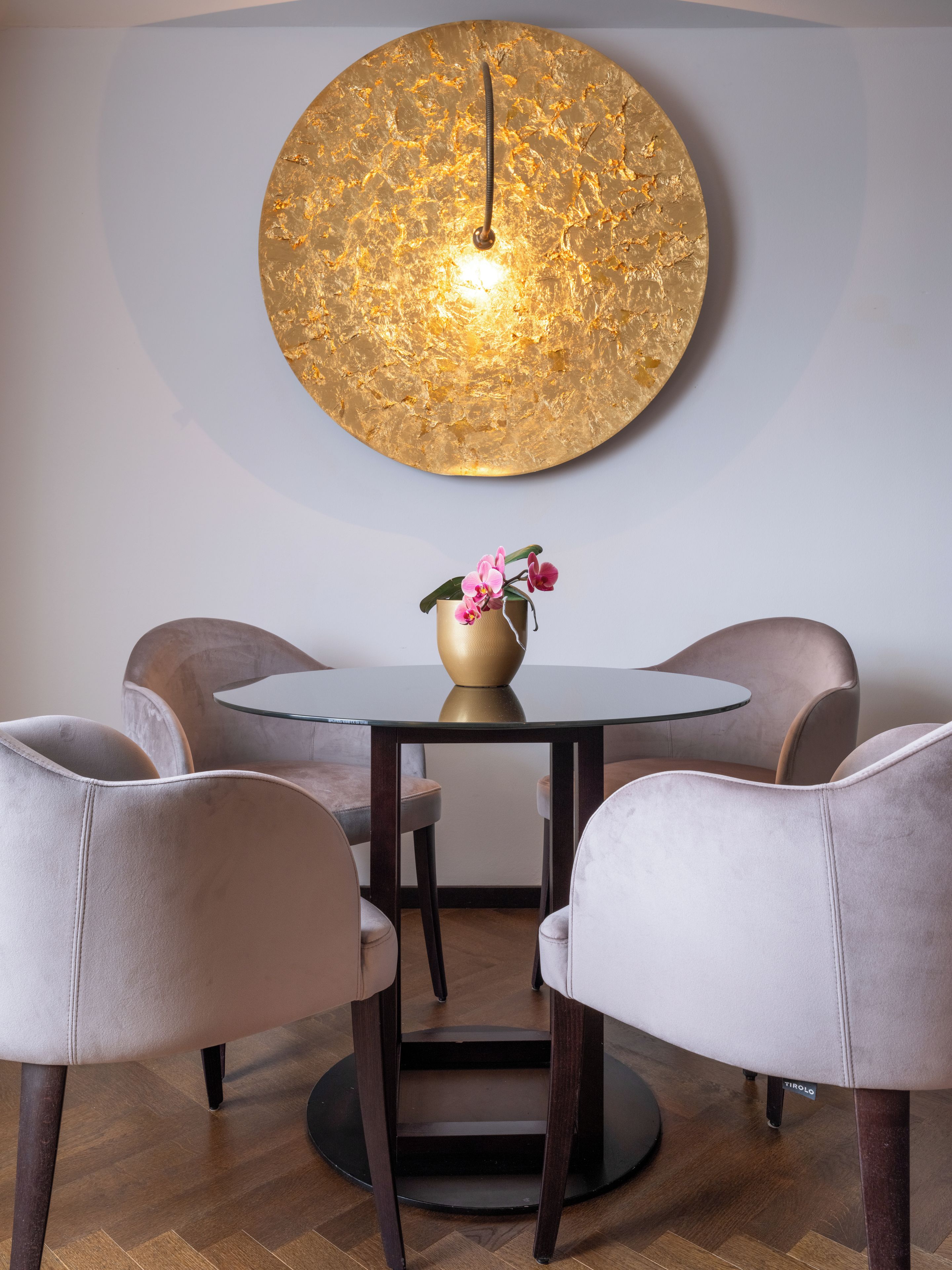 A dining area with a round table, four chairs, and a wall-mounted light fixture.