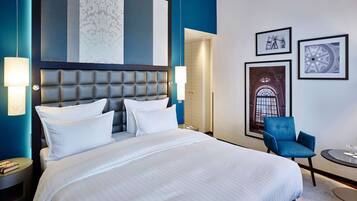 Quarto de hotel moderno com uma cama grande, uma parede azul de destaque e obras de arte emolduradas na parede.