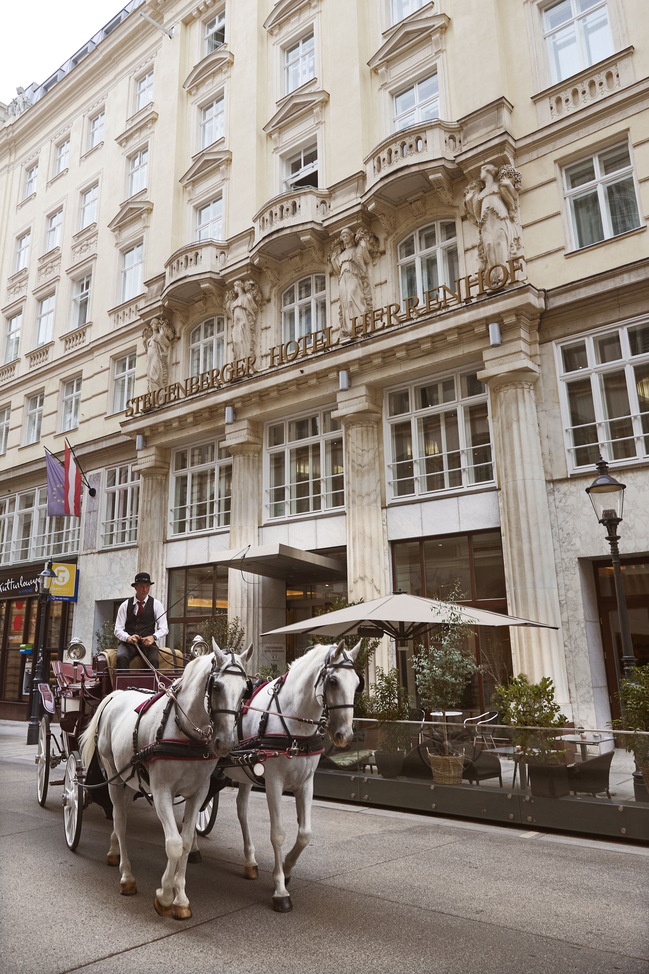 Un edificio storico con architettura elaborata, una carrozza trainata da cavalli e posti a sedere all'aperto.